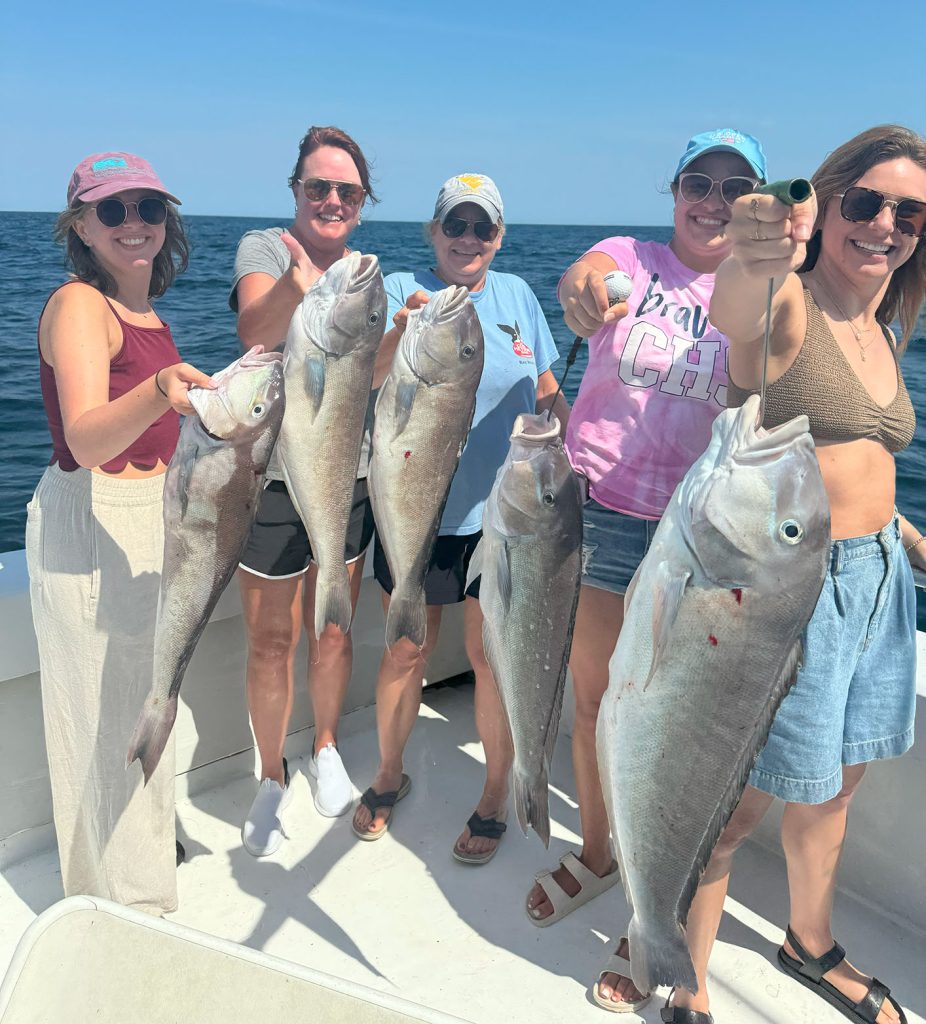 Five people on an MD fishing charter in Ocean City proudly hold up large fish they caught. Smiling, they're dressed casually in summer attire with the vast ocean as their backdrop.