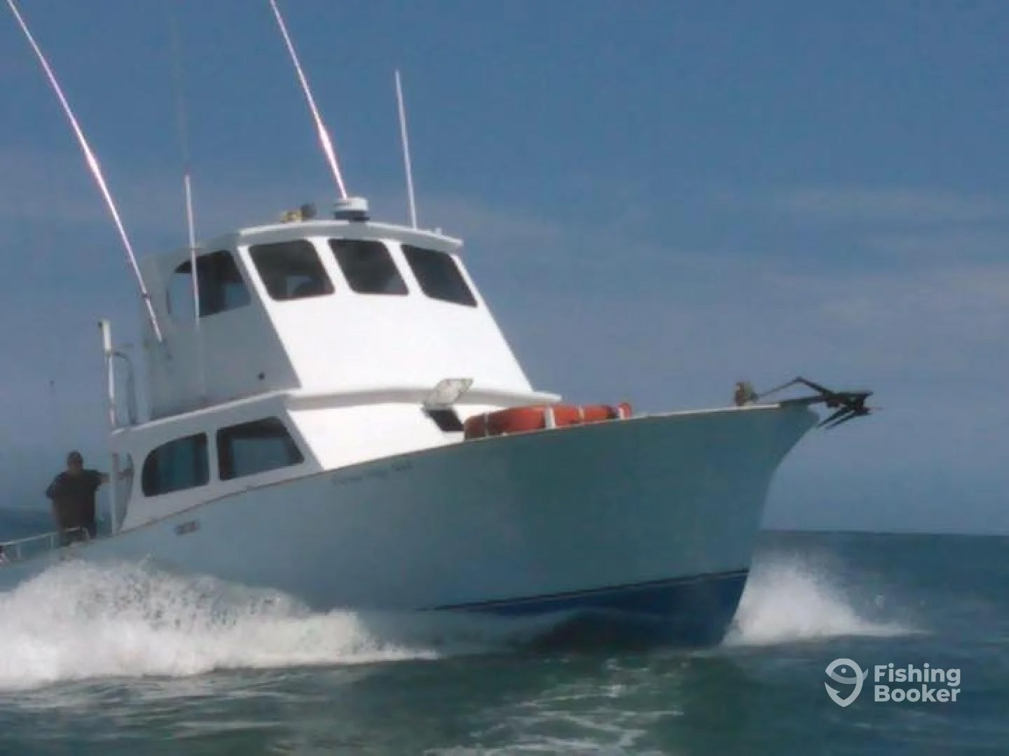 A white fishing boat with red buoys on the bow cruises through the water near Ocean City, MD, against a clear blue sky. The boat has a cabin with windows, antennas, and a person visible near the rear as part of this tranquil fishing charter. The ocean surface is lightly rippled.